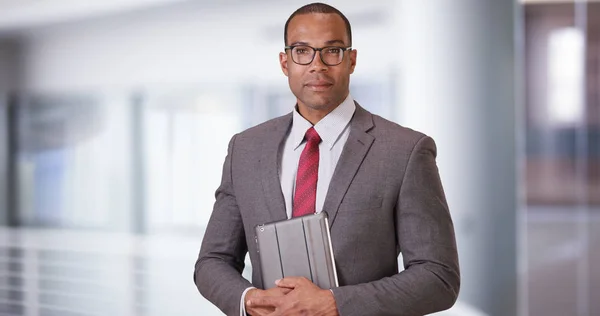 A black business professional poses for a portrait with his tablet and glasses