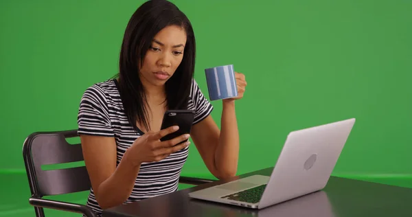 黑色女性与咖啡使用手机坐在绿色屏幕上的笔记本电脑 — 图库照片