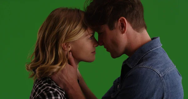 Young white couple looking into each other's eyes ready to kiss on green screen