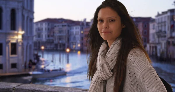 Millennial woman traveling in Italy smiles at camera by Grand Canal in evening