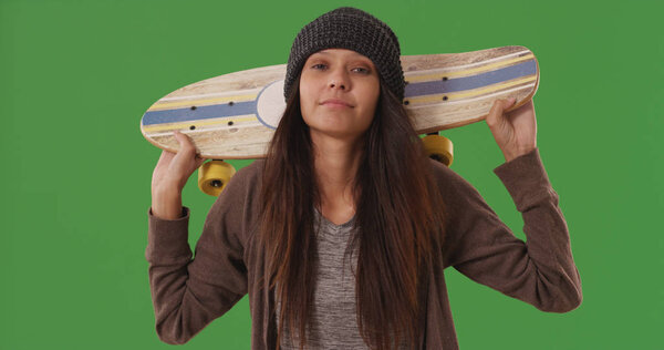 Portrait of cool skater girl carrying skateboard on shoulders on green screen