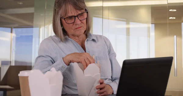 White female corporate employee eating while using laptop in office setting