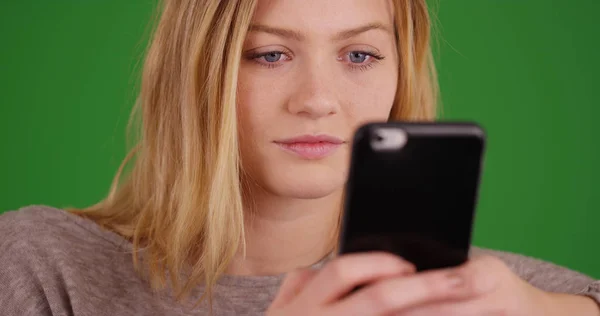 Millennial girl using cellular phone to send text messages on green screen