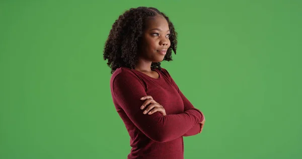 Young black woman standing with arms crossed looking offscreen on green screen
