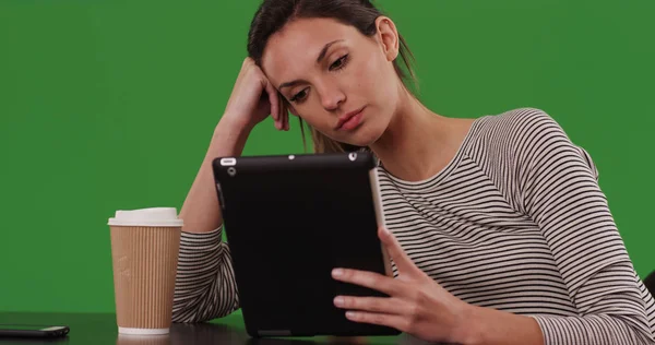 Millennial woman sitting at cafe table with tablet computer on green screen