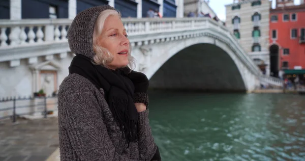 Mature woman in sweater and scarf looking out over canal on venice vacation