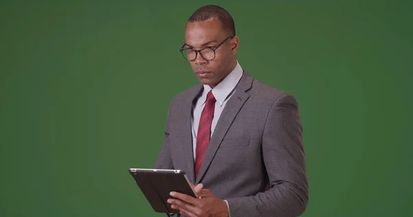 A black executive man does work on his tablet on green screen