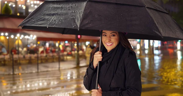 Pretty Latina woman in the city standing under umbrella