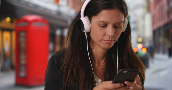 Millennial woman texts on mobile phone while listening to music  in London