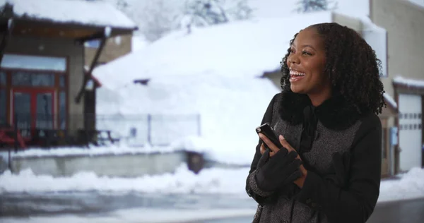 Smiling Black woman in stylish coat holding phone on winter day