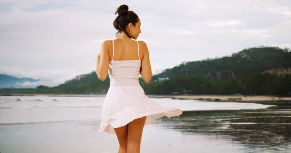 A Latina woman stands in the waves while the wind is blowing