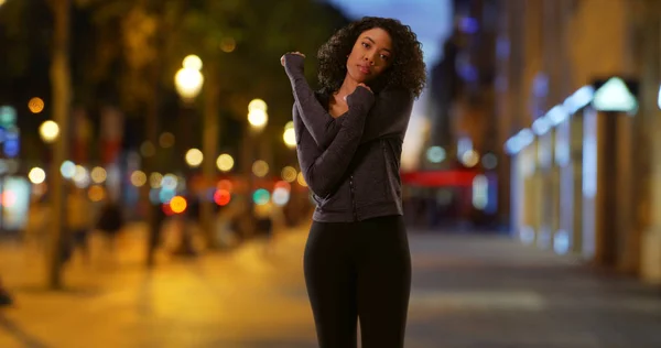 Portrait of black woman athlete on city street at night stretching