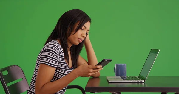 黑人妇女坐在与笔记本电脑使用智能手机在绿色屏幕上的侧面配置文件 — 图库照片