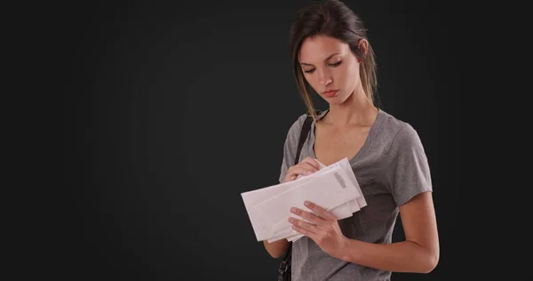 Young Caucasian woman looking through mail she received on dark gray background