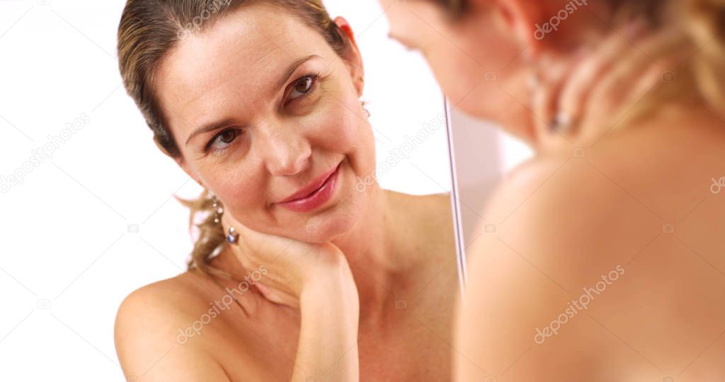 Close up of attractive middle aged Caucasian woman touching her eyes in mirror