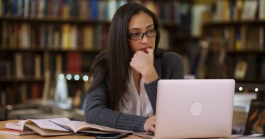 Latina üniversite öğrencisi dizüstü bilgisayarda kütüphanede çalışıyor.