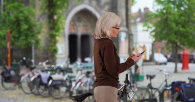 Mutlu büyük beyaz bir kadın smartphone tatile Bruges'de kullanarak Bisiklet