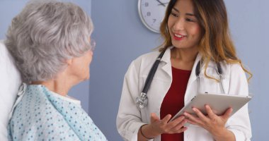 Yatakta yaşlı kadın konuşurken tablet bilgisayar kullanarak Asya hekim