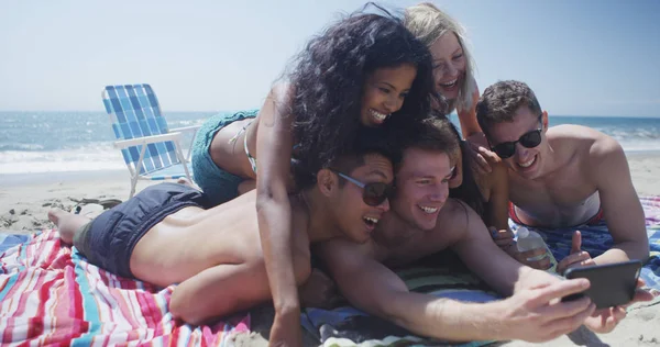 Young adult group of interracial friends lying taking selfie on the beach