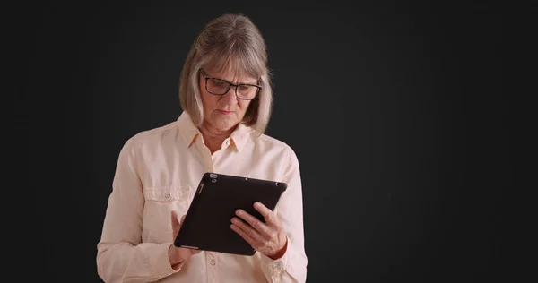 独立的高级妇女使用平板设备在灰色背景下在线浏览 — 图库照片