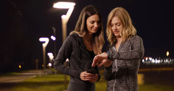 两个有魅力的女性计时慢跑 晚上在外面有停止手表和智能手机 — 图库照片