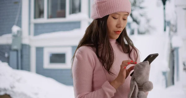 Close up of Asian millennial using smartphone on snow covered street