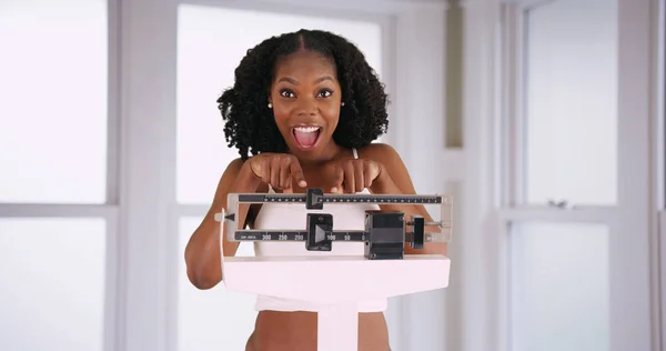 Attractive smiling black woman cheers at weight loss pointing at scale happily