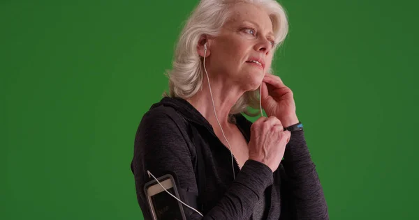 Athletic senior female putting in earphones before going on jog on green screen