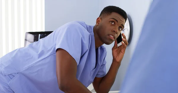 African American male doctor on mobile talking to colleague and using computer