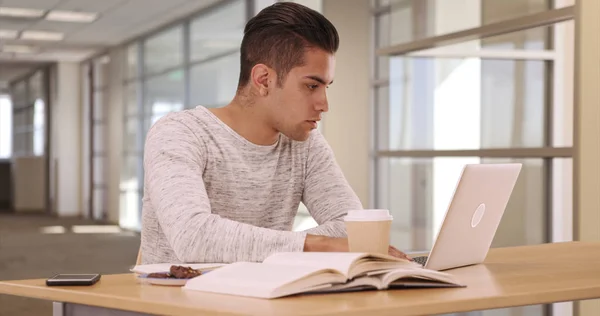 Millennial Latino university student in dorm working on laptop