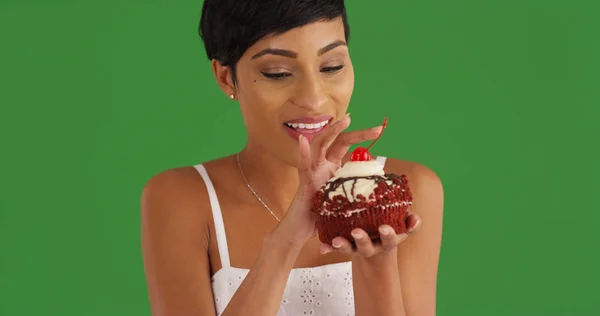 緑色の画面で赤いビロードのカップケーキを楽しむ魅力的な黒人女性 — ストック写真
