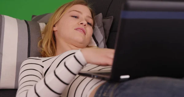 緑色の画面でノート パソコンを使用してソファの上に横になっている金髪女性のポートレート クローズ アップ — ストック写真