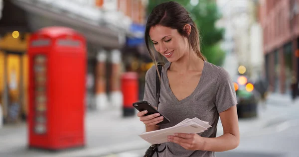 Woman with mail checking smartphone and walking offscreen in London street