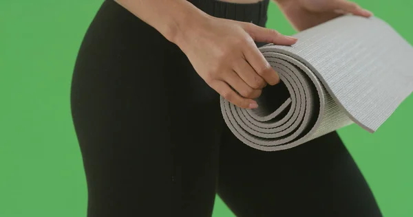 Close-up of black girl in yoga pants ready to roll out yoga mat on green screen