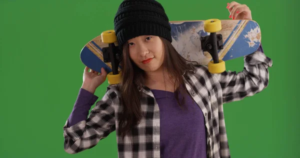 在绿色屏幕上肩上携带滑板的亚洲年轻女子 — 图库照片