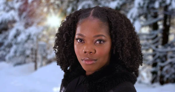 Close up of black woman standing in snowy forest sunlight shining through trees