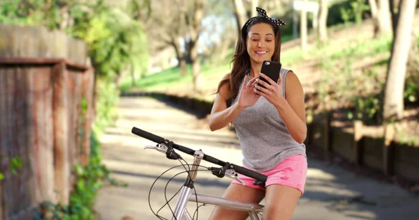 Uśmiechający Się Latina Kobieta Siedząc Rowerze Słonecznym Parku Wiadomości Telefon — Zdjęcie stockowe