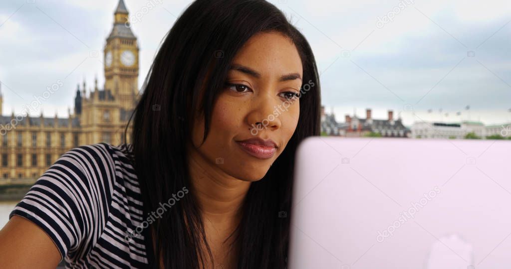 Close up of attractive black woman sitting near the Big Ben working on laptop