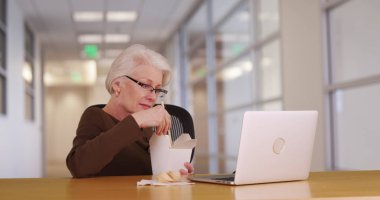 Eski beyaz kadın ofis çalışanı üzerinde laptop bir şey izlerken onun öğle yemeği molası