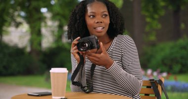 Fotoğraf makinesi ile fotoğraf çekmeye sevimli siyah kadın Bruges güzel bahçede oturur
