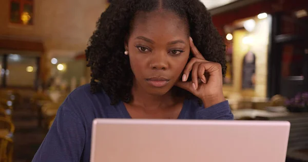 Unhappy black woman has to work on vacation using laptop at cafe in Bruges