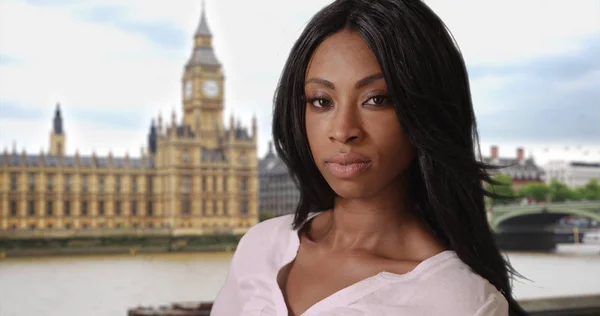 Young black female in London near Big Ben looks mysteriously at camera