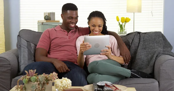 愉快的年轻黑人夫妇笑了并且使用平板电脑在沙发上 — 图库照片