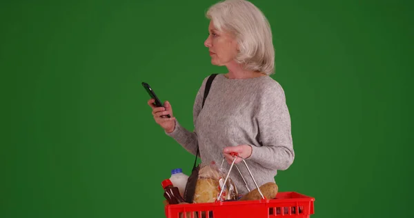 成熟的女性使用智能手机 而在绿色屏幕上的杂货店购物 — 图库照片