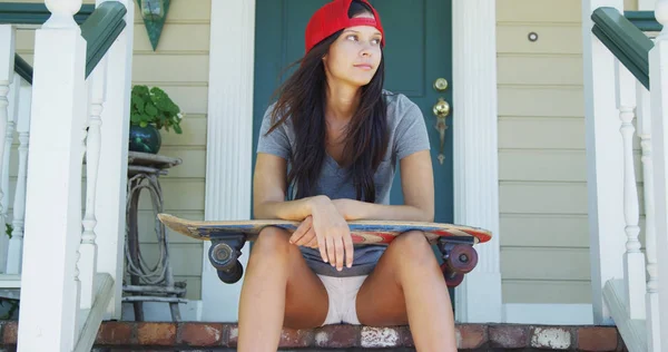 Young woman sitting on porch with skateboard