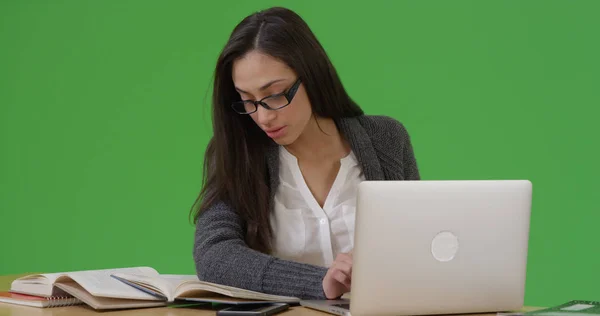 Hispanic female student typing paper on her laptop on green screen