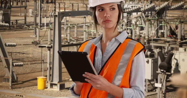 Focused female electrical worker at work on pad device at electrical facility