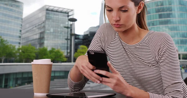 首都圏の設定で携帯電話とカフェ テーブル テキスト メッセージで座っている若い女性 — ストック写真