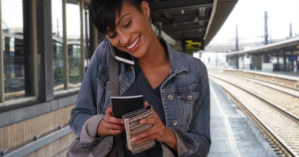 Traveling black female waiting at metro station with passport chats on smartphone