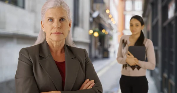 Confident serious mature woman executive and her assistant on city street